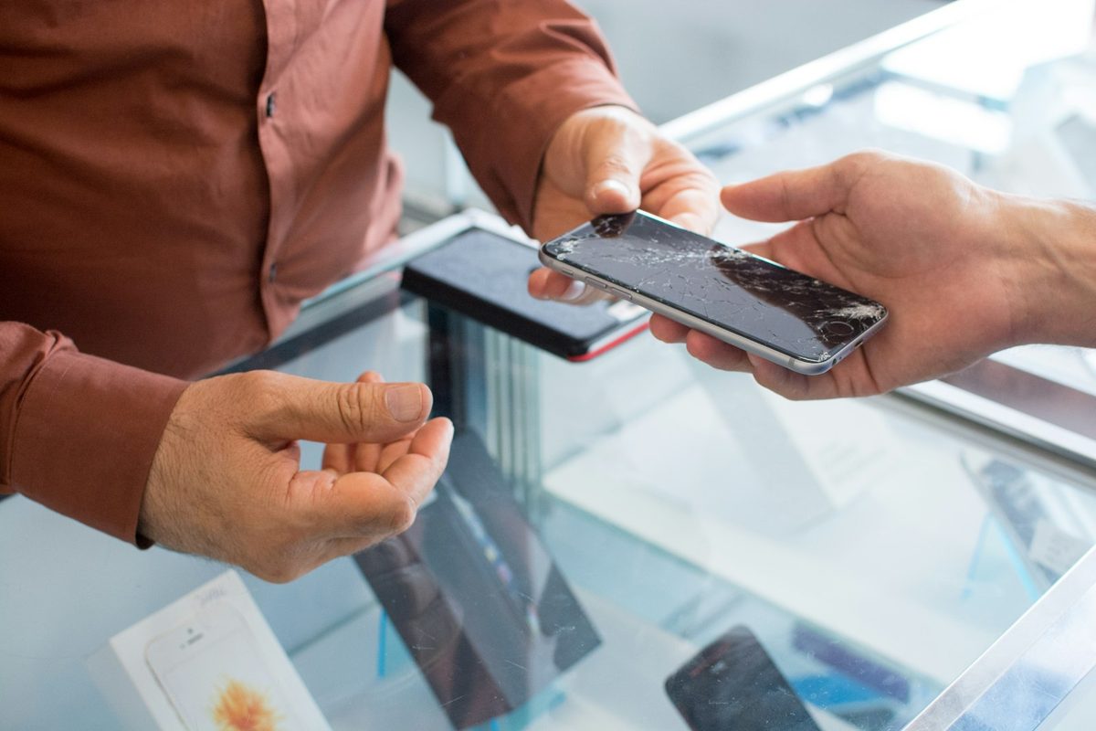 A customer handing a phone with a cracked screen across the counter