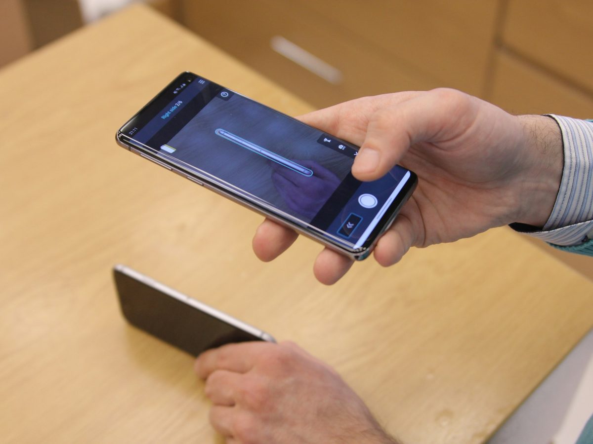 A technician holding a repaired phone and checking its screen at the workbench