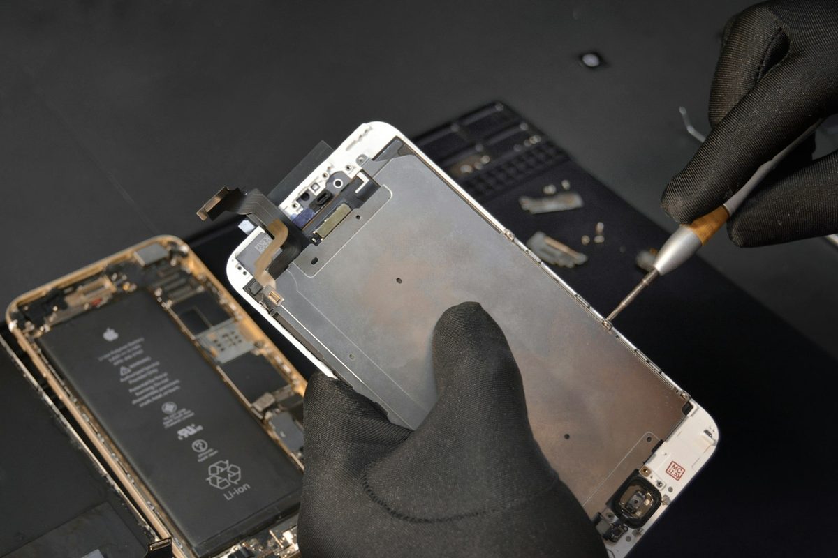 Gloved hands lifting the screen off a phone during a repair